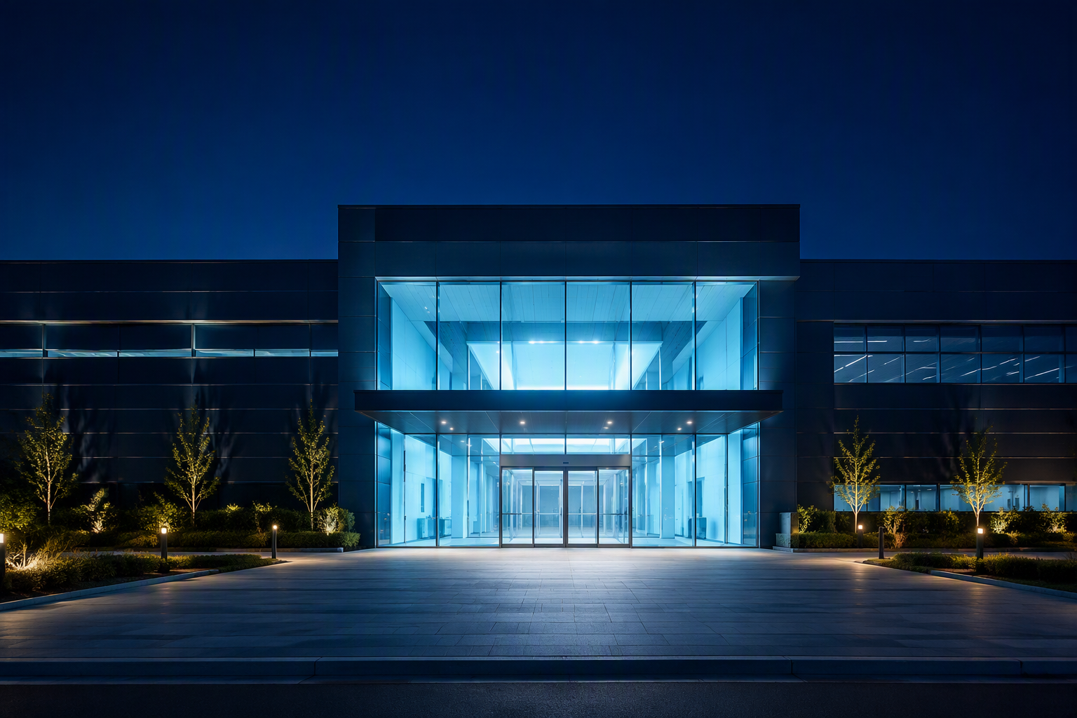 Modern electronics factory building exterior with glowing glass entrance at dusk